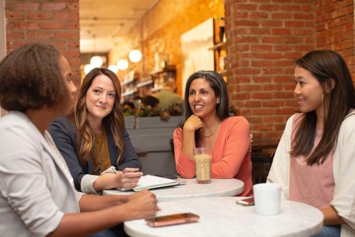 A diverse group of women engaged in an open conversation at a cafe table, symbolizing the importance of community and shared experiences in discussing health topics like urinary incontinence.