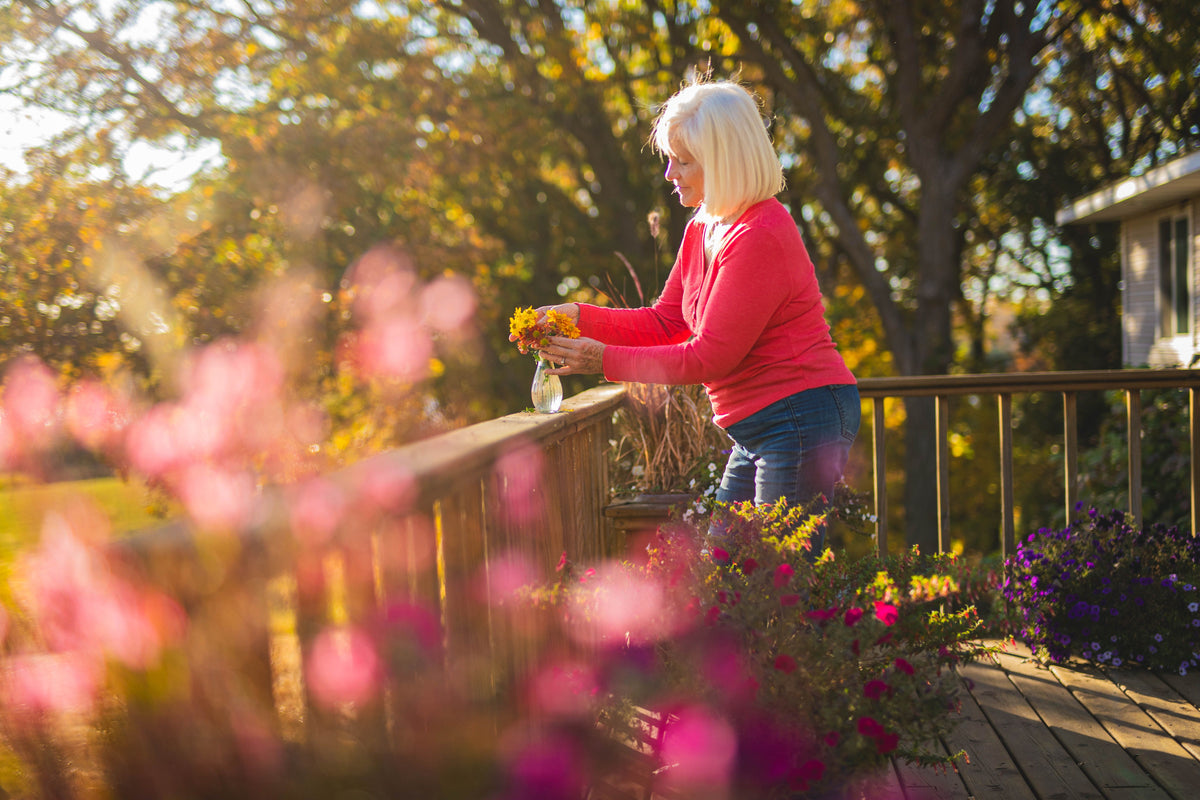 Mature woman enjoying natural bladder health and wellness while arranging flowers on a sunny deck.