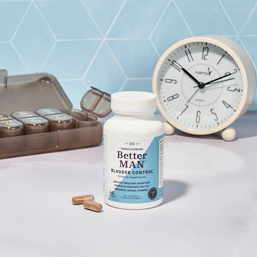 BetterMAN herbal bladder control supplement bottle with capsules, shown alongside a daily pill organizer and a clock, highlighting a consistent daily wellness routine for men.